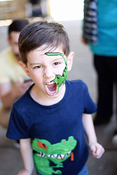 child's face painting of a dinosaur